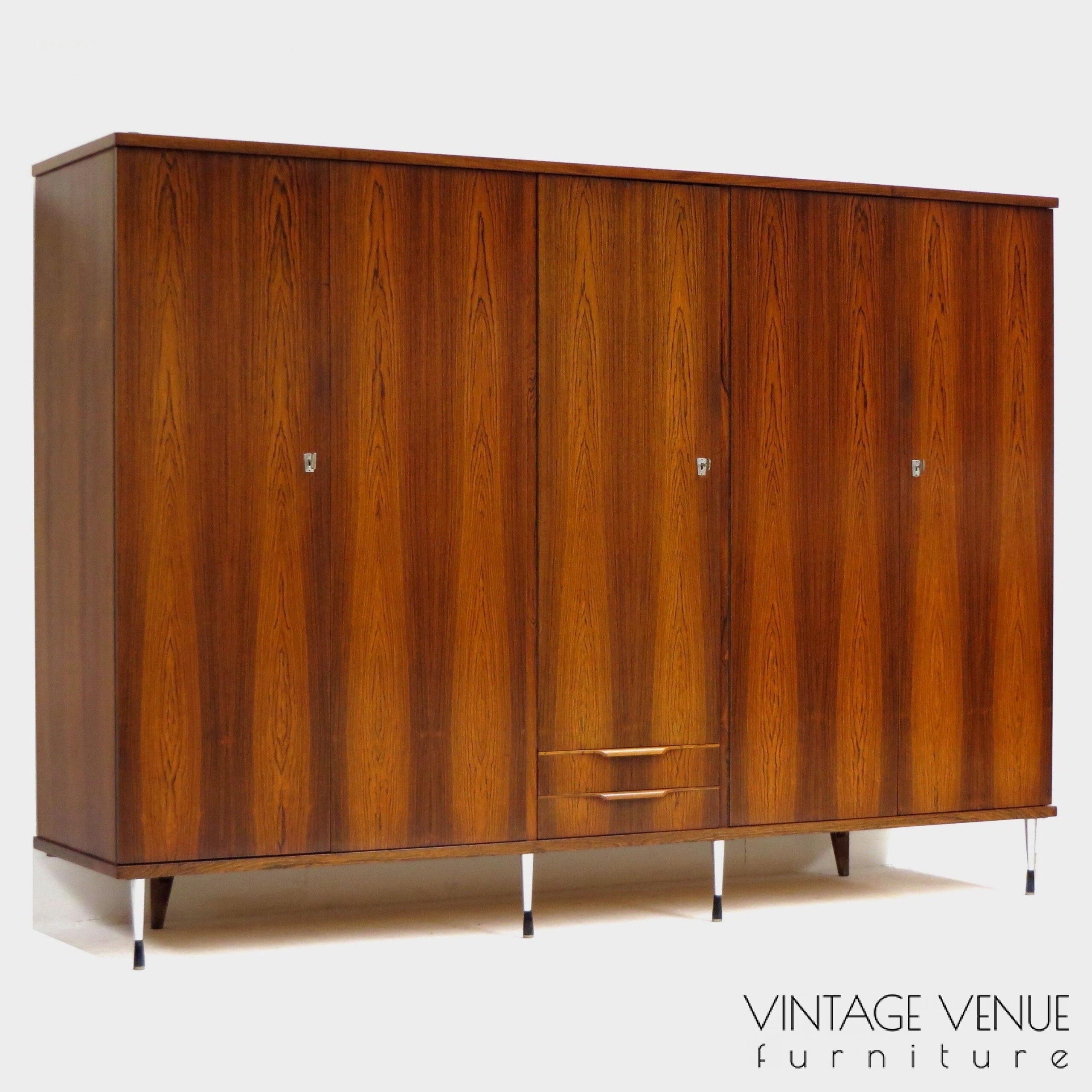 EN: 5-door vintage designer wardrobe in high quality rosewood rosewood, with stylish adjustable legs, 2 drawers with pretty handles, 4 shelves, 2 brass hanging rails, a mirror, and very sturdy adjustable & stylish metal legs. Period: 1960s. Condition: fully functional working and generally in good condition. Slight signs of use commensurate with age. ENG: Rare and exclusive high quality vintage mid century modern design wardrobe made of rosewood / rosewood. It has 5 doors, 2 drawers with beautiful carved handles, 4 shelves, 2 brass hang supports, a mirror and adjustable stylish and very solid metal legs. Period: 1960s. Condition: fully functional and overall in good condition. Light wear consistent with age and use.