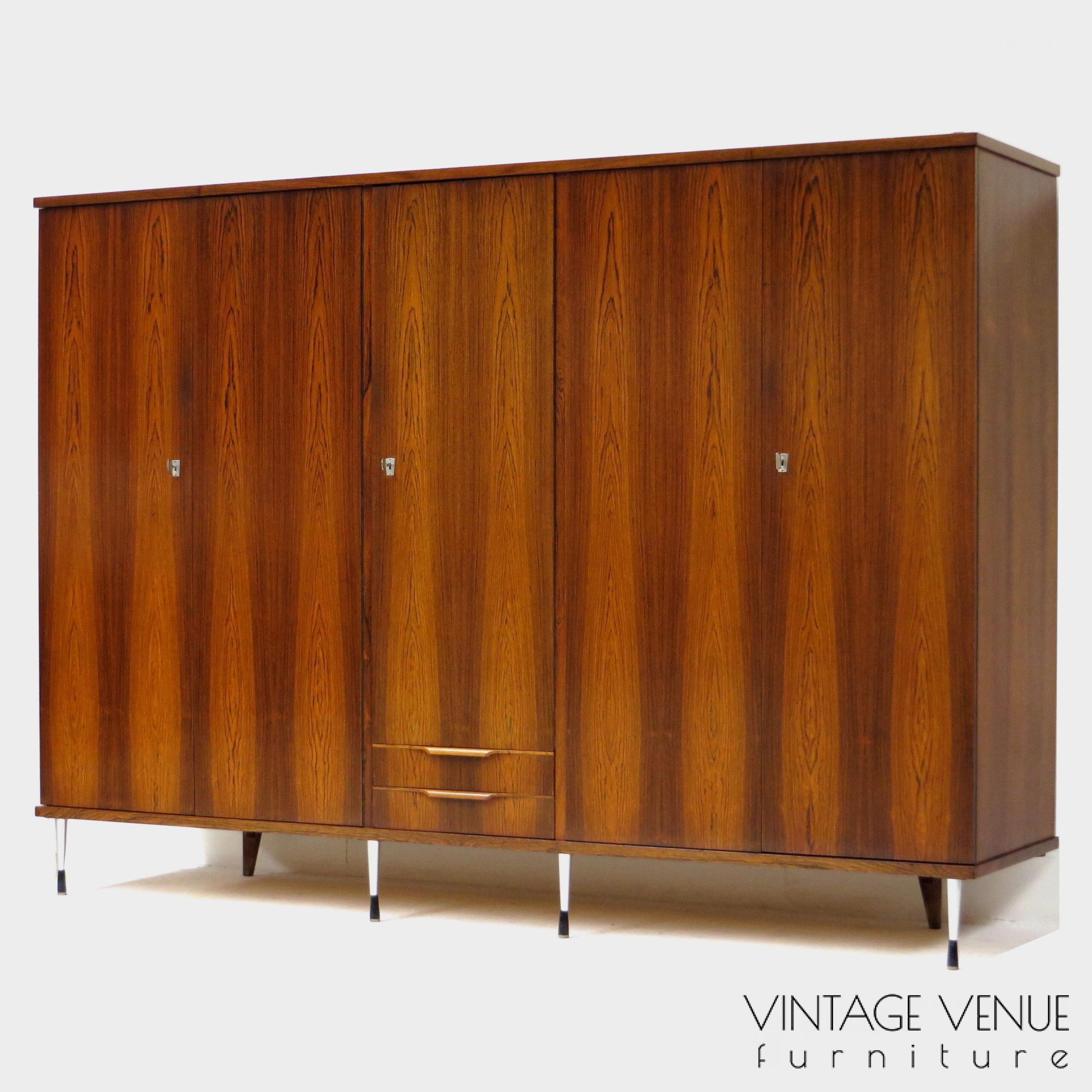 EN: 5-door vintage designer wardrobe in high quality rosewood rosewood, with stylish adjustable legs, 2 drawers with pretty handles, 4 shelves, 2 brass hanging rails, a mirror, and very sturdy adjustable & stylish metal legs. Period: 1960s. Condition: fully functional working and generally in good condition. Slight signs of use commensurate with age. ENG: Rare and exclusive high quality vintage mid century modern design wardrobe made of rosewood / rosewood. It has 5 doors, 2 drawers with beautiful carved handles, 4 shelves, 2 brass hang supports, a mirror and adjustable stylish and very solid metal legs. Period: 1960s. Condition: fully functional and overall in good condition. Light wear consistent with age and use. EN: 5-door vintage designer wardrobe in high quality rosewood rosewood, with stylish adjustable legs, 2 drawers with pretty handles, 4 shelves, 2 brass hanging rails, a mirror, and very sturdy adjustable & stylish metal legs. Period: 1960s. Condition: fully functional working and generally in good condition. Slight signs of use commensurate with age. ENG: Rare and exclusive high quality vintage mid century modern design wardrobe made of rosewood / rosewood. It has 5 doors, 2 drawers with beautiful carved handles, 4 shelves, 2 brass hang supports, a mirror and adjustable stylish and very solid metal legs. Period: 1960s. Condition: fully functional and overall in good condition. Light wear consistent with age and use.