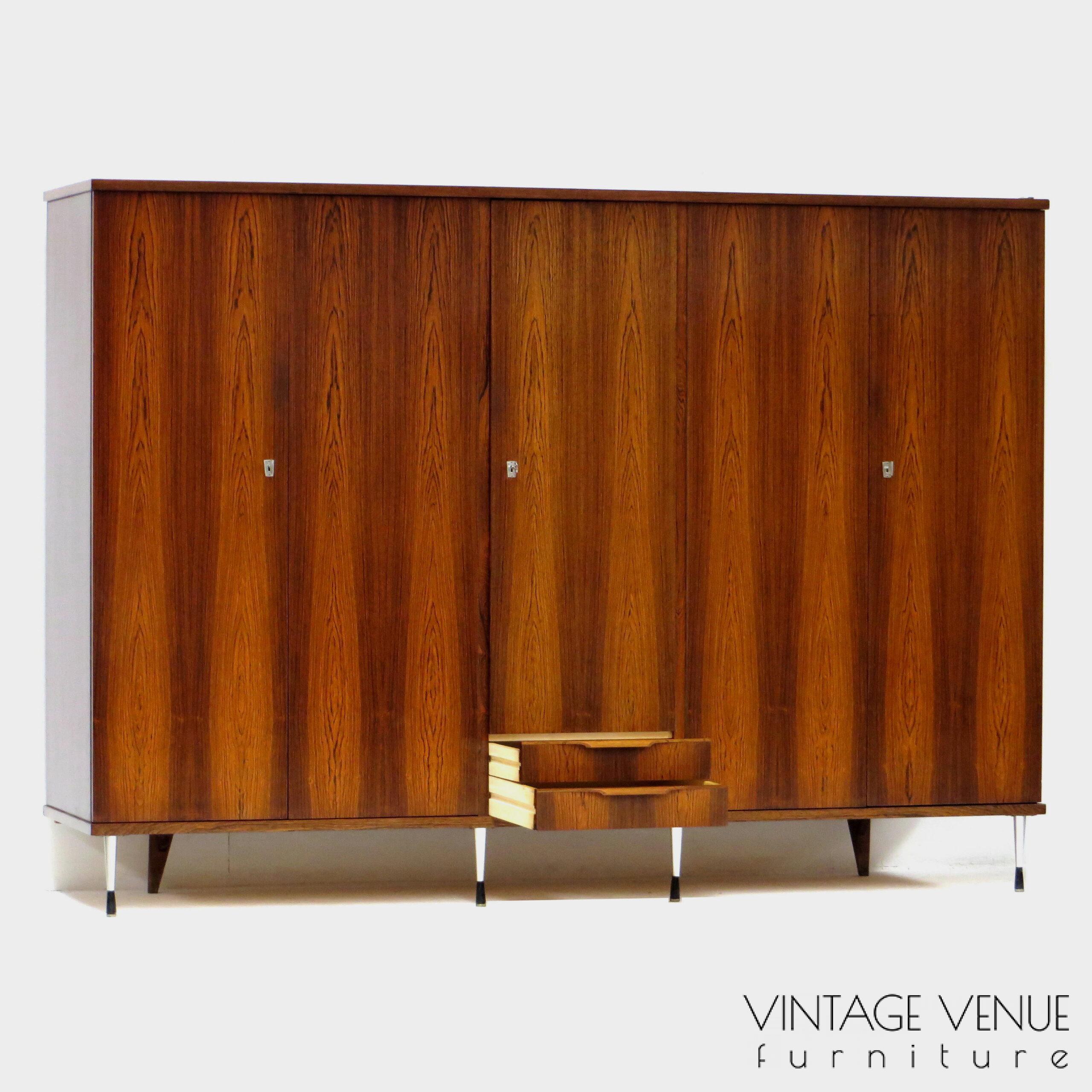EN: 5-door vintage designer wardrobe in high quality rosewood rosewood, with stylish adjustable legs, 2 drawers with pretty handles, 4 shelves, 2 brass hanging rails, a mirror, and very sturdy adjustable & stylish metal legs. Period: 1960s. Condition: fully functional working and generally in good condition. Slight signs of use commensurate with age. ENG: Rare and exclusive high quality vintage mid century modern design wardrobe made of rosewood / rosewood. It has 5 doors, 2 drawers with beautiful carved handles, 4 shelves, 2 brass hang supports, a mirror and adjustable stylish and very solid metal legs. Period: 1960s. Condition: fully functional and overall in good condition. Light wear consistent with age and use. EN: 5-door vintage designer wardrobe in high quality rosewood rosewood, with stylish adjustable legs, 2 drawers with pretty handles, 4 shelves, 2 brass hanging rails, a mirror, and very sturdy adjustable & stylish metal legs. Period: 1960s. Condition: fully functional working and generally in good condition. Slight signs of use commensurate with age. ENG: Rare and exclusive high quality vintage mid century modern design wardrobe made of rosewood / rosewood. It has 5 doors, 2 drawers with beautiful carved handles, 4 shelves, 2 brass hang supports, a mirror and adjustable stylish and very solid metal legs. Period: 1960s. Condition: fully functional and overall in good condition. Light wear consistent with age and use.
