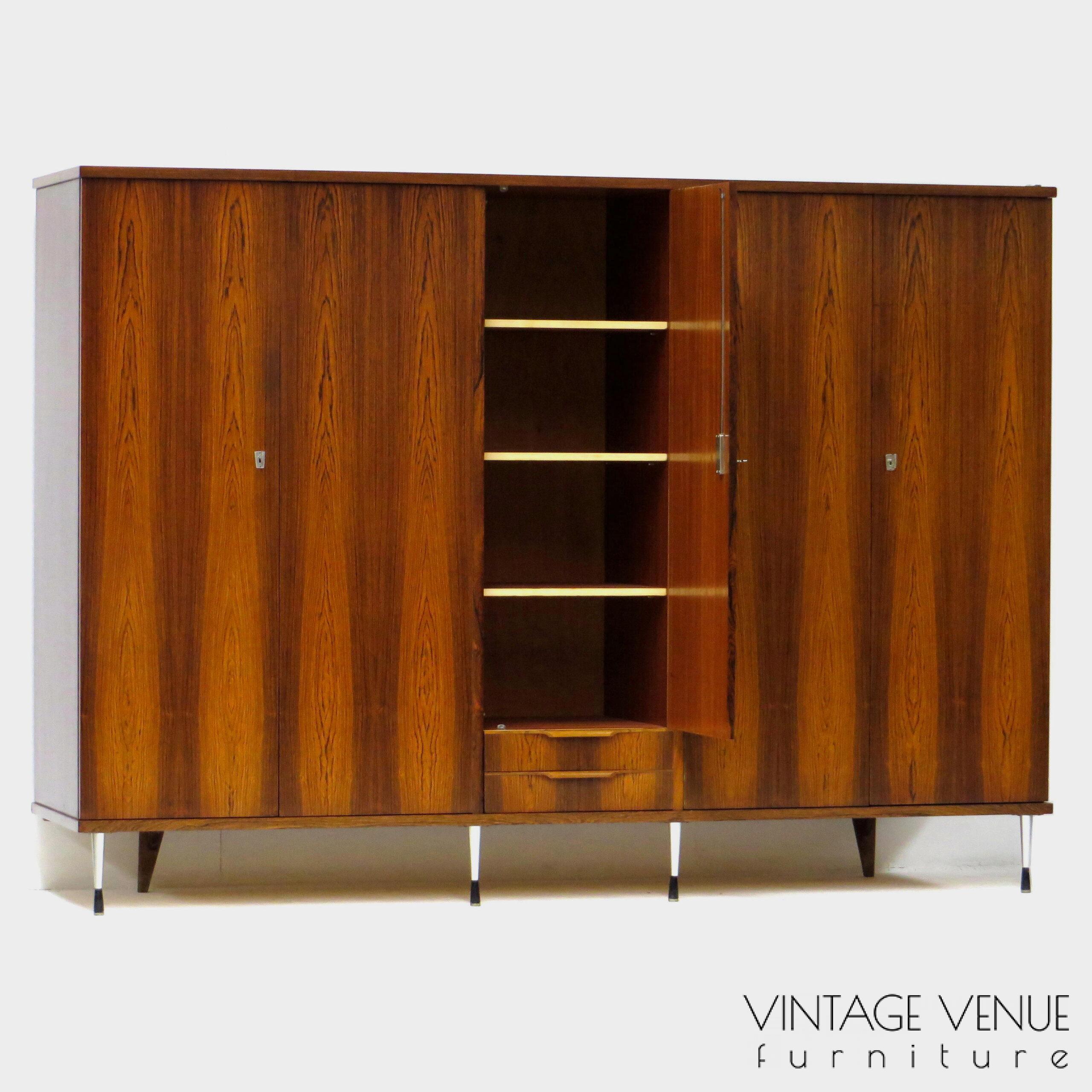 EN: 5-door vintage designer wardrobe in high quality rosewood rosewood, with stylish adjustable legs, 2 drawers with pretty handles, 4 shelves, 2 brass hanging rails, a mirror, and very sturdy adjustable & stylish metal legs. Period: 1960s. Condition: fully functional working and generally in good condition. Slight signs of use commensurate with age. ENG: Rare and exclusive high quality vintage mid century modern design wardrobe made of rosewood / rosewood. It has 5 doors, 2 drawers with beautiful carved handles, 4 shelves, 2 brass hang supports, a mirror and adjustable stylish and very solid metal legs. Period: 1960s. Condition: fully functional and overall in good condition. Light wear consistent with age and use. EN: 5-door vintage designer wardrobe in high quality rosewood rosewood, with stylish adjustable legs, 2 drawers with pretty handles, 4 shelves, 2 brass hanging rails, a mirror, and very sturdy adjustable & stylish metal legs. Period: 1960s. Condition: fully functional working and generally in good condition. Slight signs of use commensurate with age. ENG: Rare and exclusive high quality vintage mid century modern design wardrobe made of rosewood / rosewood. It has 5 doors, 2 drawers with beautiful carved handles, 4 shelves, 2 brass hang supports, a mirror and adjustable stylish and very solid metal legs. Period: 1960s. Condition: fully functional and overall in good condition. Light wear consistent with age and use.
